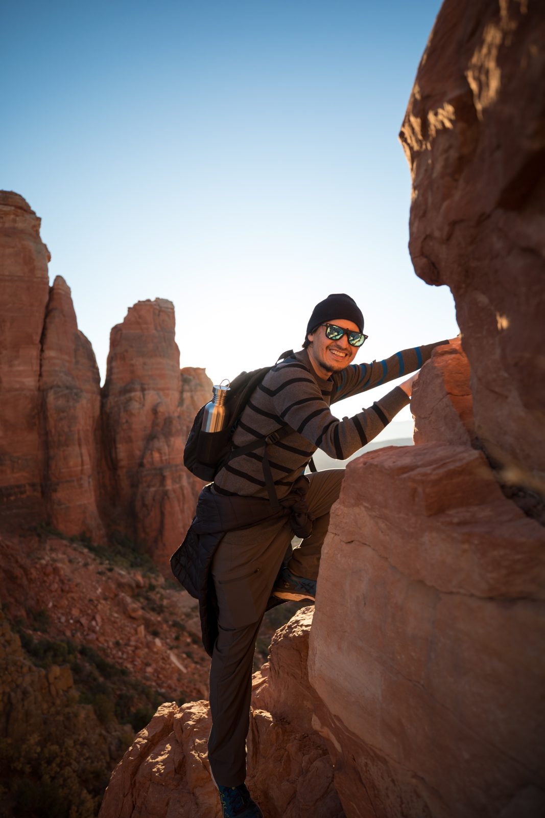 Hiker scrambling up a red rock formation in Sedona on a sunny day
